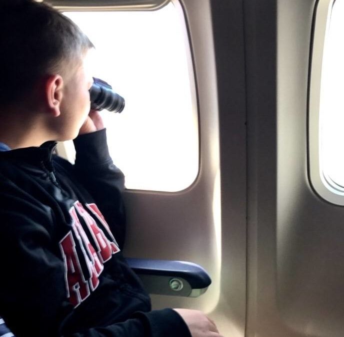 Life that Counts - Boy looking out of a plane with binoculars.